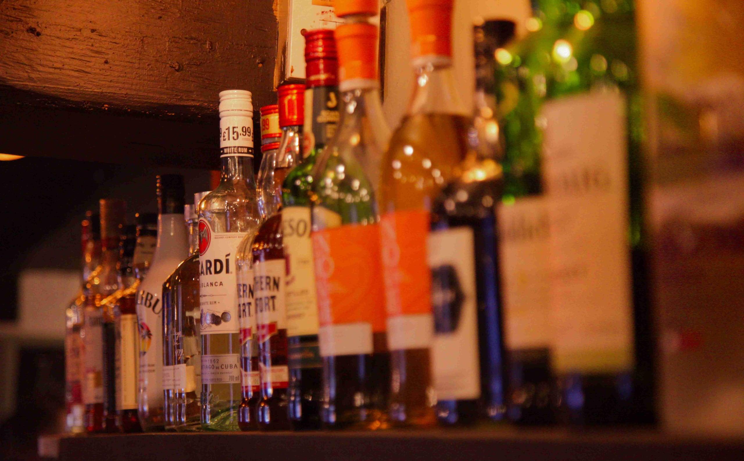 A row of spirits on the pub's back-bar shelf, lit warmly against exposed timber.